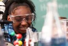 Photo of a smiling student wearing protective eyewear in science class with beakers in foreground