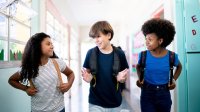 Photo of three smiling middle school students walking together down hallway