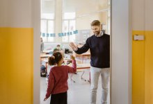 Photo of teacher greeting female student with a high-five at class door