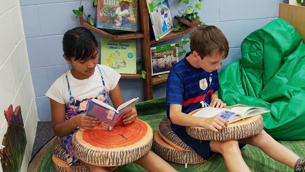 A boy and girl sit together reading separate books in the class climate change corner