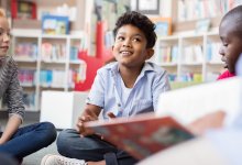 Students listening to teacher read a book while sitting on the floor