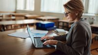 Teacher working on laptop at her desk in empty classroom