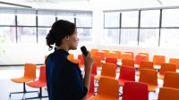 how to make conference presentation Woman practicing giving a speech to an empty room with orange seats