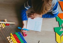 Child writing math equations surrounded by manipulatives