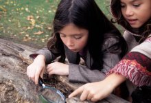 photo of two girls using magnify glass on log