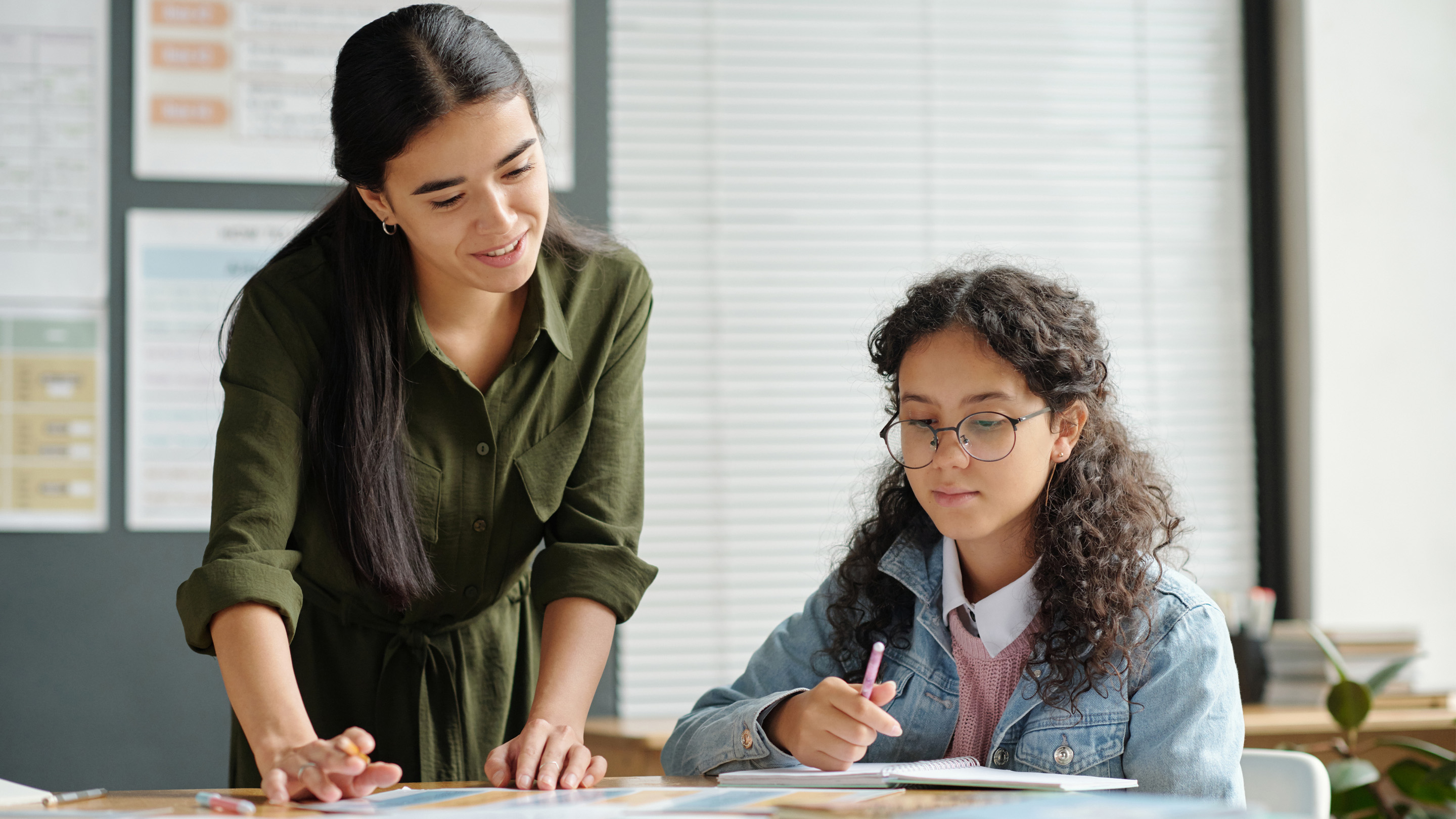 A teacher sitting with a foster youth in a classroom, reviewing homework together.
