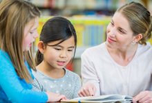 Teacher listening to two students read a book