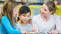 Teacher listening to two students read a book