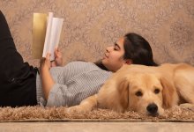 Girl reading book leaning on dog