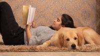 Girl reading book leaning on dog