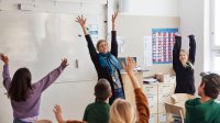 Photo of school teacher and students raising both hands in classroom