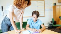 elementary school teacher assisting student with sentence stem writing