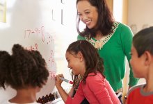 Photo of elementary school teacher and students writing math equations on whiteboard