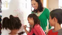 Photo of elementary school teacher and students writing math equations on whiteboard