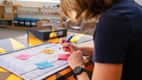 A teacher is writing out school events on sticky notes to attach to a calendar