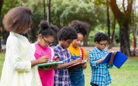 A group of elementary students standing outside writing in notebooks to celebrate the spring equinox