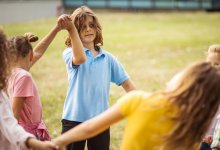 A photo of elementary students outdoors and holding hands in a circle completing a P.E game