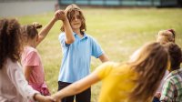 A photo of elementary students outdoors and holding hands in a circle completing a P.E game