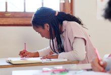 A female black high schooler focused on note-taking in class