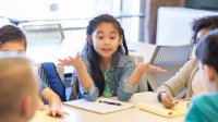 A group of elementary students in a circle engaging in a discussion while one student leads