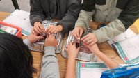A photo of four students working together to light a lightbulb with a battery, representing supporting English learners in science classes
