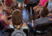 A photo of students sitting in a circle while participating in a discussion led by a teacher
