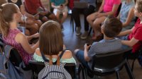 A photo of students sitting in a circle while participating in a discussion led by a teacher