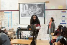 Two students projecting an image of two female scientists while presenting in front of their classmates