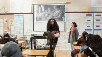 Two students projecting an image of two female scientists while presenting in front of their classmates