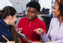 A photo of a teacher supervising a discussion among two middle school students