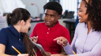 A photo of a teacher supervising a discussion among two middle school students