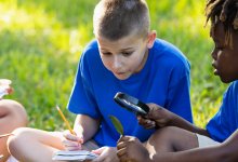 A photo of two students outdoors observing and making notes of a leaf