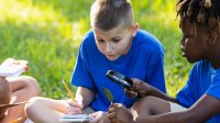 A photo of two students outdoors observing and making notes of a leaf