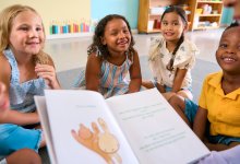 An image of elementary students sitting in a circle and looking engaged as their teacher reads them a picture book out loud.