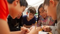 A photo of five elementary students talking while huddled in a circle over a math worksheet.