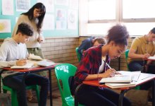 An image of a middle school teacher looking over her students as they write in their journals.
