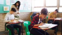 An image of a middle school teacher looking over her students as they write in their journals.