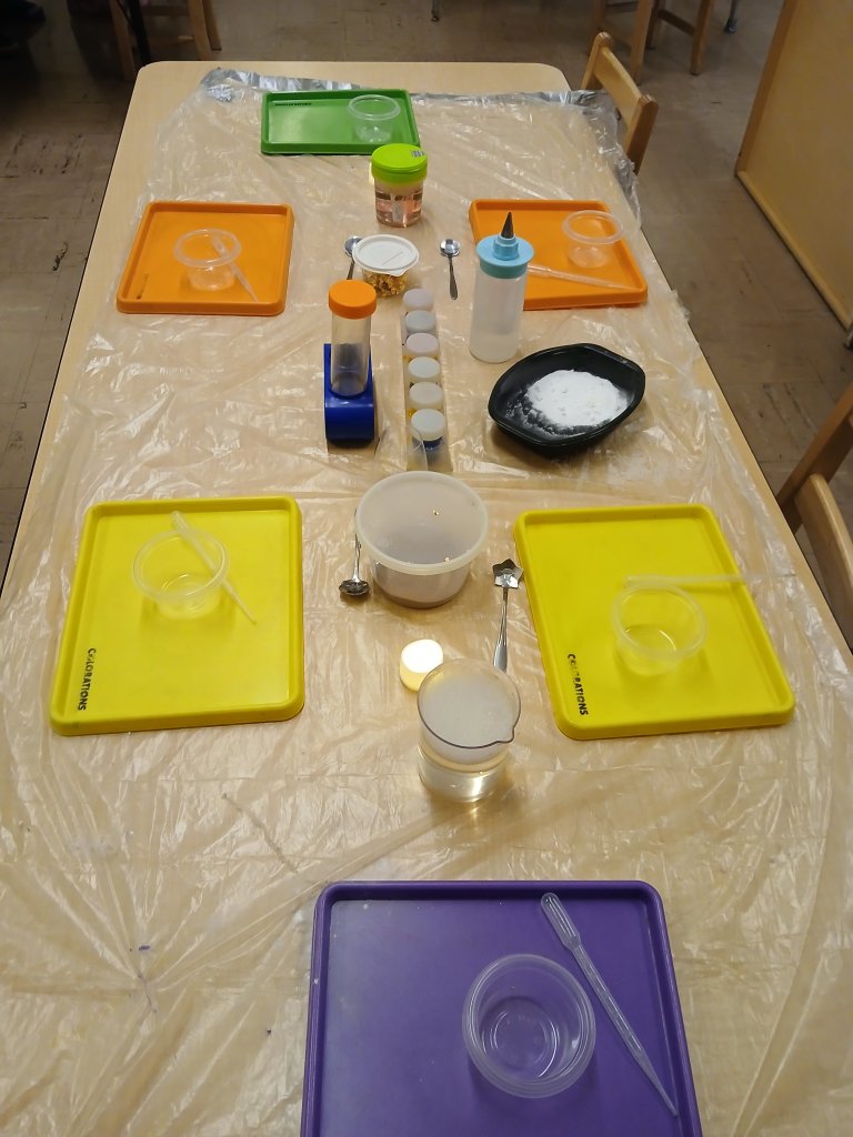 An image of a a classroom table set up with colorful trays surrounding different types of containers