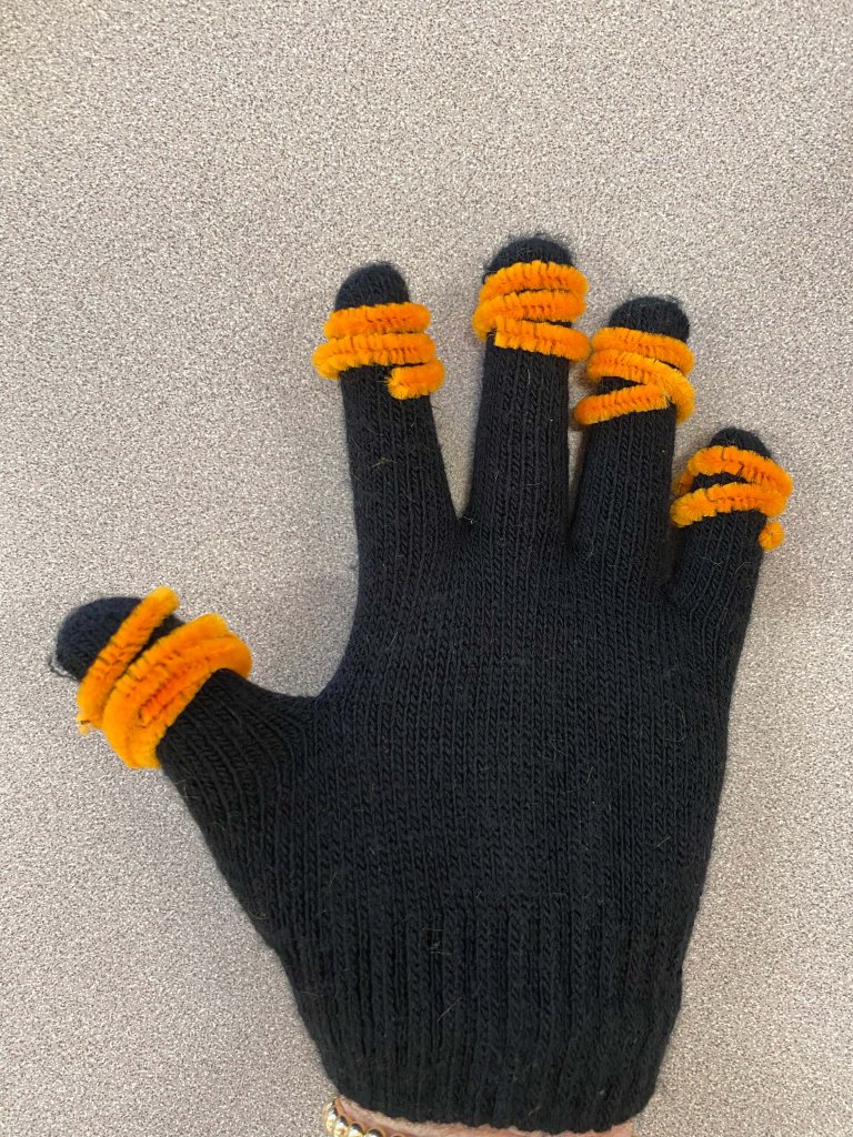 An image of a black glove with orange pipe cleaners wrapped around each finger to resemble pumpkins