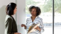 A photo of two school leaders standing by a window and engaged in peer coaching.