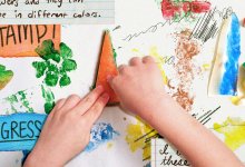 A student's hands pressing down on a carrot painted with green acrylic paint to make a print. Scattered around the hands are various stamps made from vegetables, scraps of paper, and pen doodles.