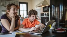 A photo of a middle school student and his mother sitting at the kitchen table closely examining the student's laptop.