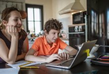 A photo of a middle school student and his mother sitting at the kitchen table closely examining the student's laptop.