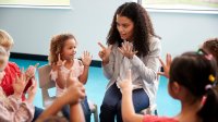 A photo of a circle of prek students following their teacher's finger counting movements.