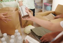 An image of two students volunteering at a fundraiser, collecting donations of food, water bottles, clothes, and cans.