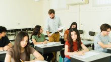 A photo of a high school teacher handing his seated students their graded assignments.