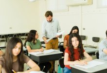 A photo of a high school teacher handing his seated students their graded assignments.