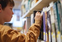 A photo of a young elementary student picking a book from a library shelf.