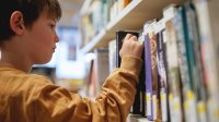 A photo of a young elementary student picking a book from a library shelf.