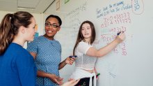 A photo of a teacher and two high school students at a whiteboard and solving algebra problems.
